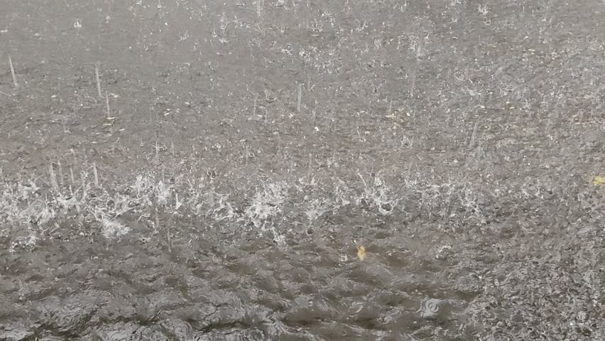 Atmospheric view of torrential rain falling on a gray pavement surface with bubbles and water spray during a heavy downpour