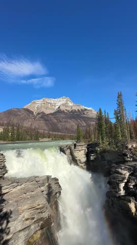Powerful Athabasca falls cascading over rocks with mountains and forest in Jasper National Park, Canada