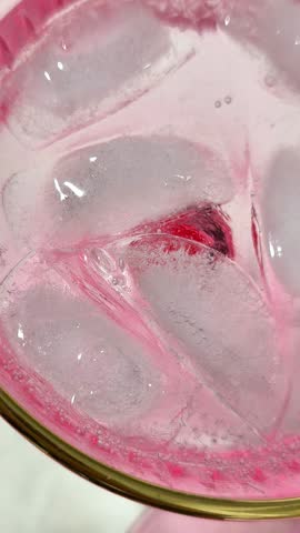 Lemon slice placed into glass with ice in indoor setting, refreshment concept. Lemon piece floats among ice cubes, citrus accent, showing preparation of cold beverage and serving process. vertical