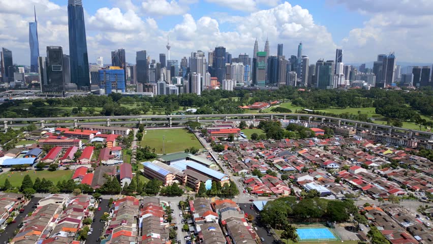 Aerial drone view of Kuala Lumpur featuring modern skyline, dense residential houses, green park area and elevated railway line. Urban cityscape showing infrastructure and development in Malaysia.
