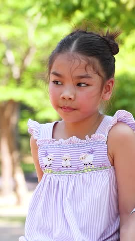 A young Asian girl in a purple dress smiles and looks around in Lumpini Park