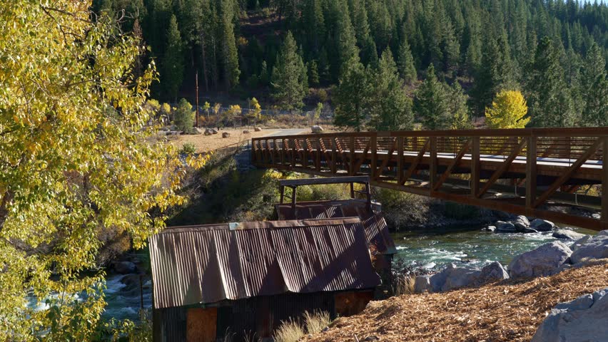 Rustic cabin beside flowing river with wooden bridge and autumn foliage