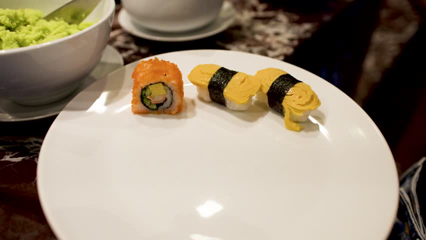 A person places a small dish and wasabi onto a plate with various sushi rolls