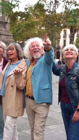 Group of stylish senior friends enjoying their vacation. Happy retired man pointing at something with his friends during a city tour