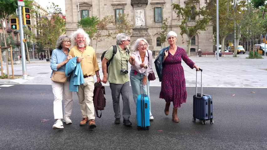 Group of smiling elderly tourists with suitcases crossing a street together. Active senior friends enjoying their vacation and exploring a city