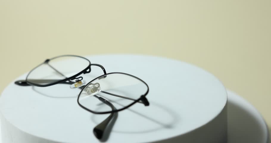 Pair of stylish eyeglasses on podium against light background, rotating