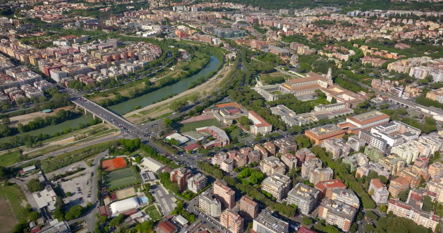 Aerial panorama of Rome, Italy, featuring the Tiber River, Marconi Bridge, and the Basilica of Saint Paul Outside the Walls amidst a dense urban layout with green spaces and residential buildings.