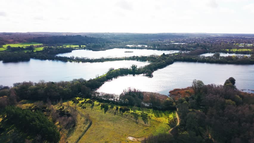 Drone view over multiple connected lakes in Somerset wetlands with tree-lined banks and open countryside creating layered water patterns