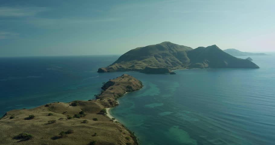 Drone aerial shot of island hills surrounded by ocean creating a scenic tropical landscape. The natural beauty and calm environment make it ideal for travel themes.