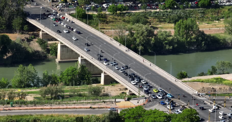 Aerial view of the Marconi Bridge in Rome, Italy, showing traffic crossing the Tiber River. The scene captures the urban infrastructure and green riverbanks of the Italian capital from above.