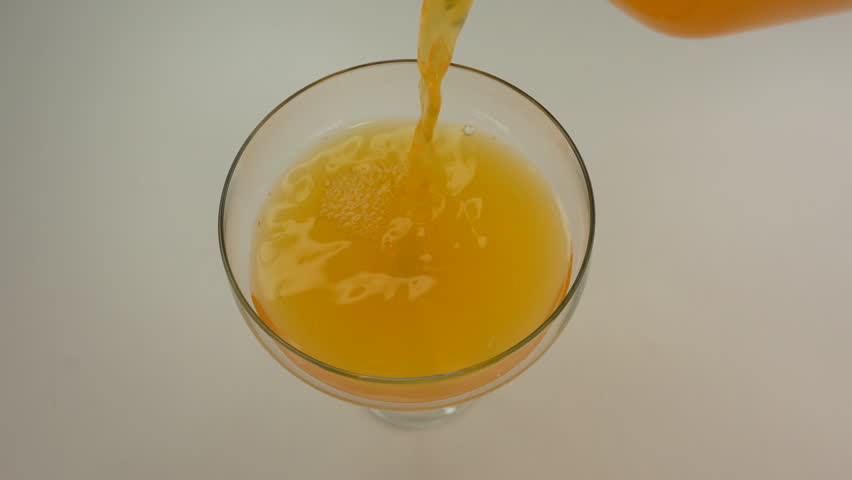 Orange juice pouring into a glass on white table. Selective focus.