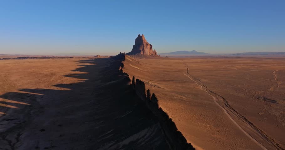 Aerial drone shot approaching Shiprock, an iconic volcanic formation in the New Mexico desert. Vast arid landscape, dramatic rock spire, and open Southwest terrain