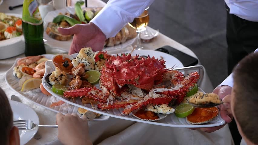 Close-up of a waiter holding a plate of crab and serving it to people in a restaurant. Large cooked crab on a plate with sauce and seasonings.