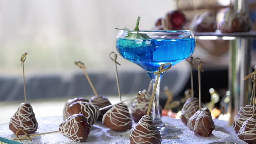 Chocolate-covered strawberries and a blue cocktail on the table in a restaurant, sweet snacks and drinks at a party.