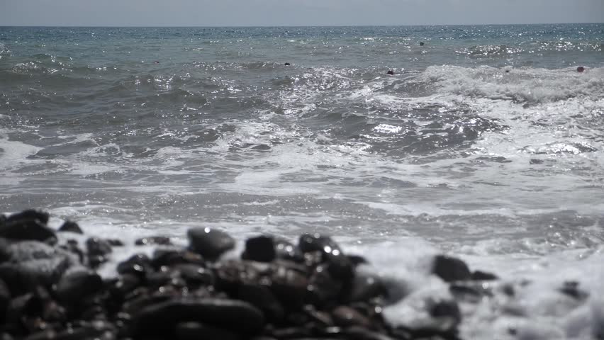 A view of large waves moving slowly. Muddy waves rise and crash against the rocky shore, forming foam. The sea during a storm.