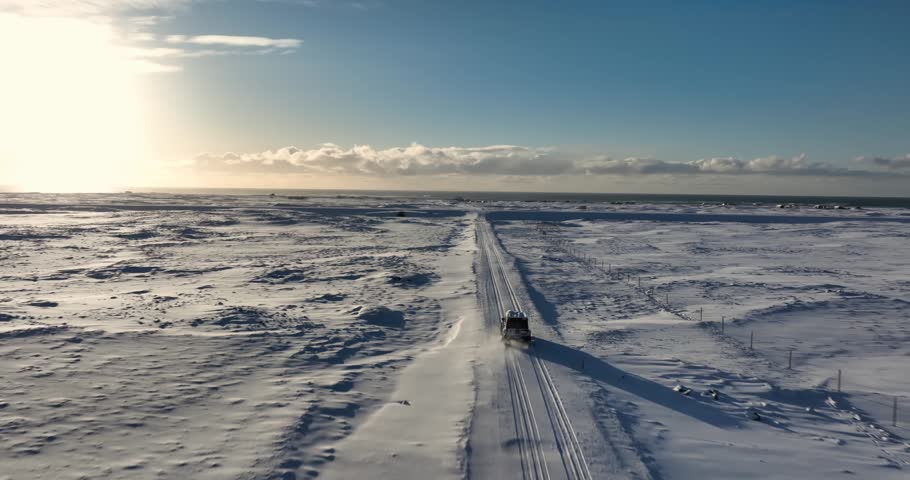 Aerial view of a lone vehicle driving across the frozen expanse near Kleifarvatn on Iceland’s Reykjanes Peninsula under bright winter sun.