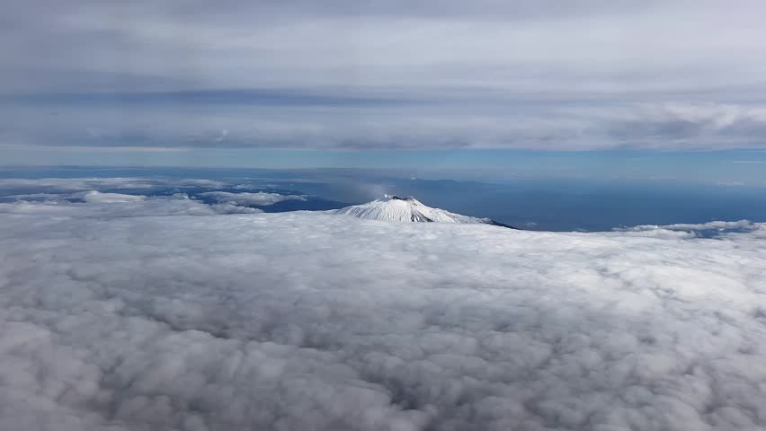 An aerial view of a volcanic crater emitting smoke; Mount Etna rises from a dense layer of clouds in the sky above the Italian island of Sicily 