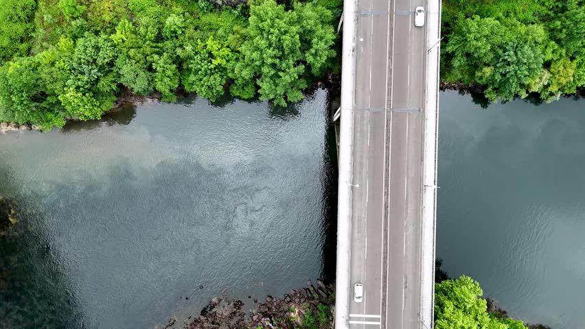 Top down aerial view of a city road bridge over a river. Cars are driving over the bridge and on a roundabout with green infrastructure