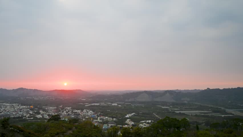 A scenic view of the sunset over the rural village of Yujing in Tainan, Taiwan, featuring rolling hills and a peaceful town landscape.