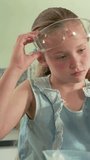Girl student lifting goggles and preparing beaker with blue liquid for science lab experiment. Child, classroom, instructor, peers, glasses, scarf, vertical video - Powered by Shutterstock - Get 15% off with code: PIKWIZARD15