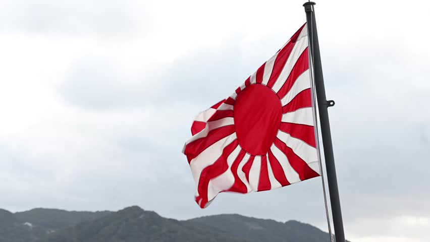 Imperial japanese navy's ensign, the rising sun flag, waving in the wind against a cloudy sky