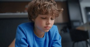 Pensive young boy with curly hair in a blue shirt looking downward indoors, captured in a quiet home kitchen with soft natural light - Powered by Shutterstock - Get 15% off with code: PIKWIZARD15