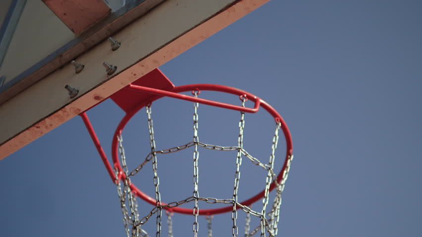 Basketball ball hitting rim of hoop, bouncing and falling into metal net, gimbal shot from behind basketball backboard. Ball landing exactly on target. Winning throw without players outdoors.