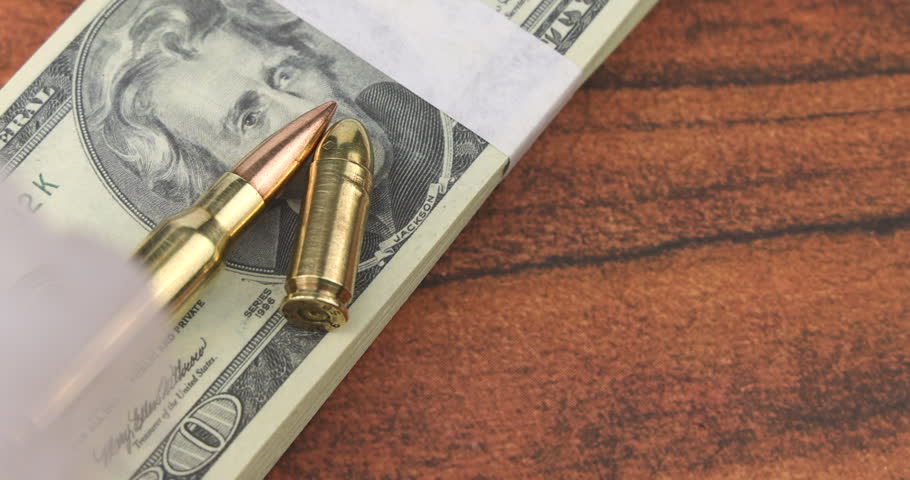 Fan of twenty dollar banknotes and a shiny rifle bullet on mahogany table through thick smoke showing the dangerous costs of weaponry.