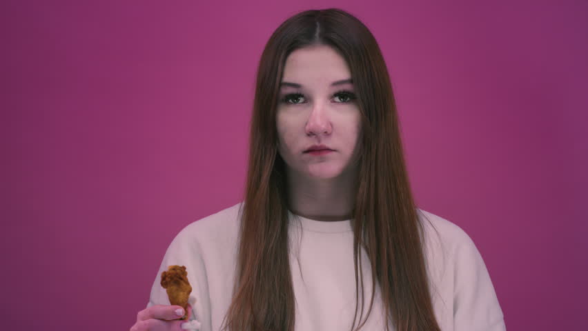 Woman eating a fried chicken wing from fast food. Teen girl bites unhealthy junk. Crispy chicken pieces, takeaway food, casual dining moment. Young female have a crispy meat.
