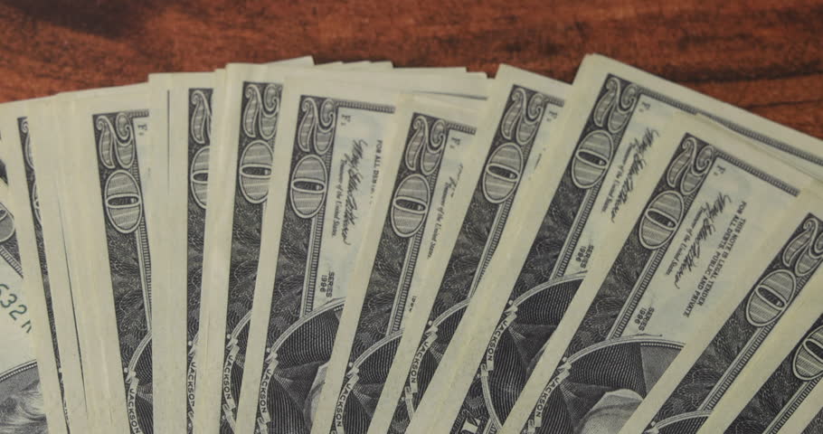 New shiny rifle bullet placed on top of twenty dollar bills fan on mahogany table symbolizing high price of war and corruption.