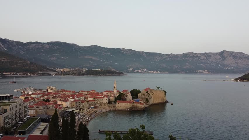 Horizontal drone video of the old town of Budva, Montenegro, featuring historic buildings, the sea, and a sunset over this popular tourist destination