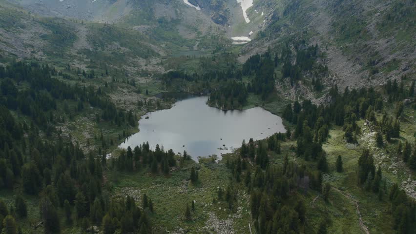 Drone footage over Karakol Lakes surrounded by rocky slopes, taiga forest and patches of snow in the Altai Mountains, Siberia, Russia, remote summer landscape