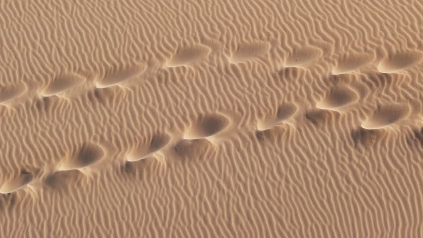 Footprints in soft sand forming textured pattern on beach or desert surface, natural background symbolizing travel, journey and human presence in a minimalistic environment