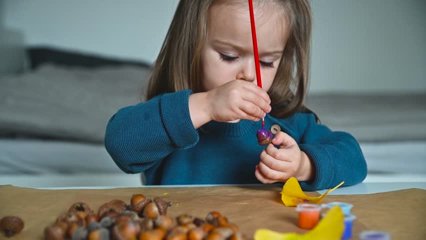 Cute toddler girl painting acorns with a brush for a craft project. Autumn creative DIY Slowmotion Full HD footage.