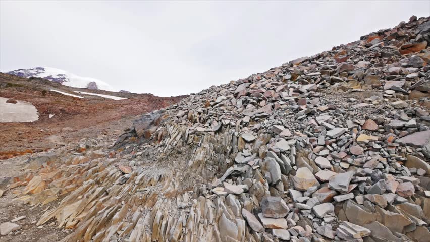A wide-angle view of the steep, rocky terrain and scree slopes along the popular Skyline Trail, leading towards Panorama Point in Mount Rainier National Park. Snow patches are visible on the reddish-b