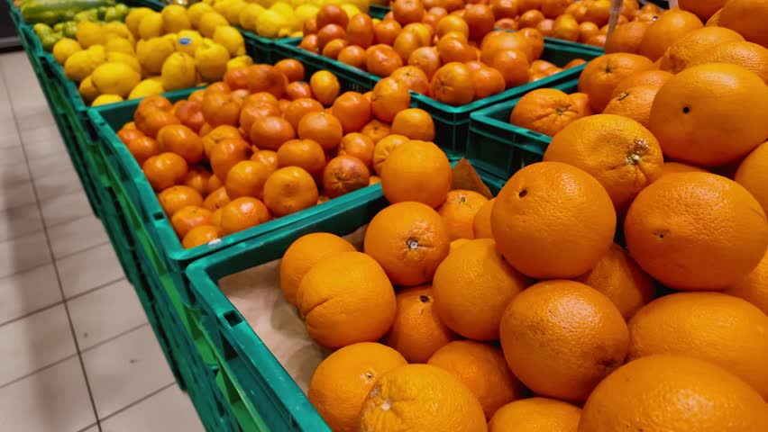 Smooth camera movement over a diverse selection of fresh fruits in green crates at a grocery store, showcasing oranges, lemons, watermelons, kiwis, and coconuts available for purchase