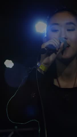 Vertical video: Female singer starting concert, singing into mic, engaging crowd hands and lights. Stage, spotlight, lensflare, intimate, live, venue, vertical video