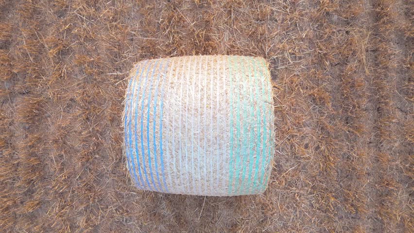 Aerial view of a single round hay bale wrapped in blue and green netting sitting in a dry harvested field in Geneva, Geneva, Switzerland.