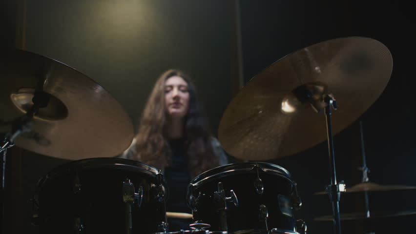 Young female drummer passionately playing a drum kit in a professional rehearsal studio, energetically striking cymbals and drums with drumsticks. Hair flying. Rock Feminist style. Woman power.