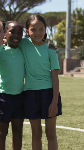Vertical video: Posing then loosening, three kids moving forward on turf, wearing green shirts. Teamwork, youth, field, outdoor, unity, motion, vertical video