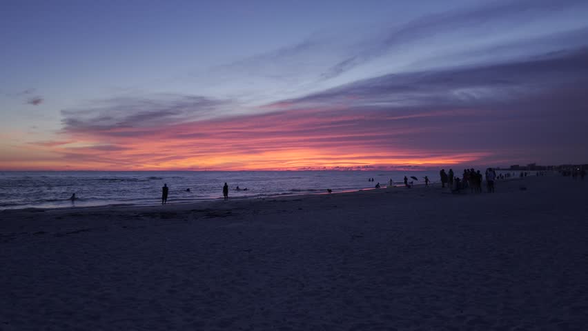 Aerial view of a vibrant sunset over the ocean with people walking on the sand at Madeira Beach, Florida, United States.