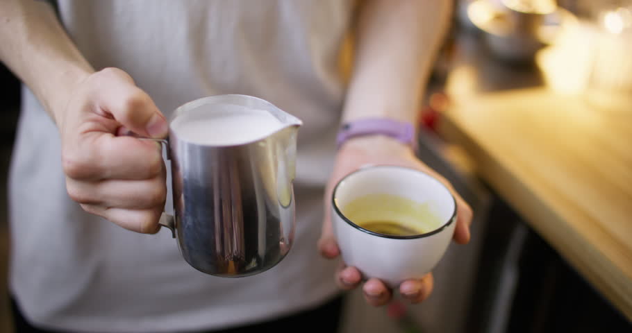 Latte art. Pouring foamed milk. Barista hand adding frothing steaming creamy liquid to aromatic beverage serving coffee in ceramic cup.