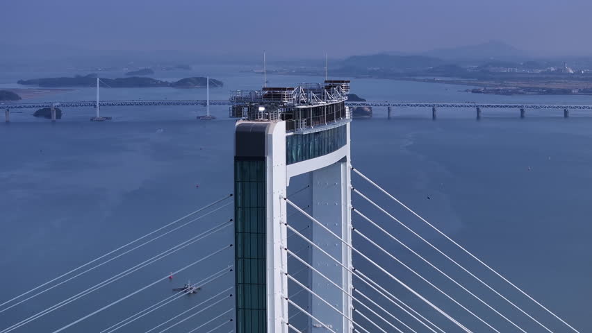 Cinematic aerial view of Cheongna Sky Bridge in Incheon, South Korea. The large cable-stayed bridge stretches across the blue sea, creating a modern coastal landscape with transportation infrastructure and ocean scenery.
