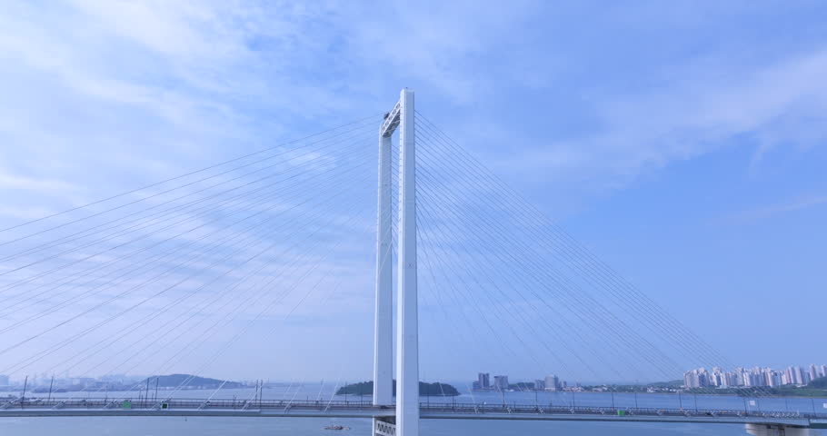 Cinematic aerial view of Cheongna Sky Bridge in Incheon, South Korea. The large cable-stayed bridge stretches across the blue sea, creating a modern coastal landscape with transportation infrastructure and ocean scenery.

