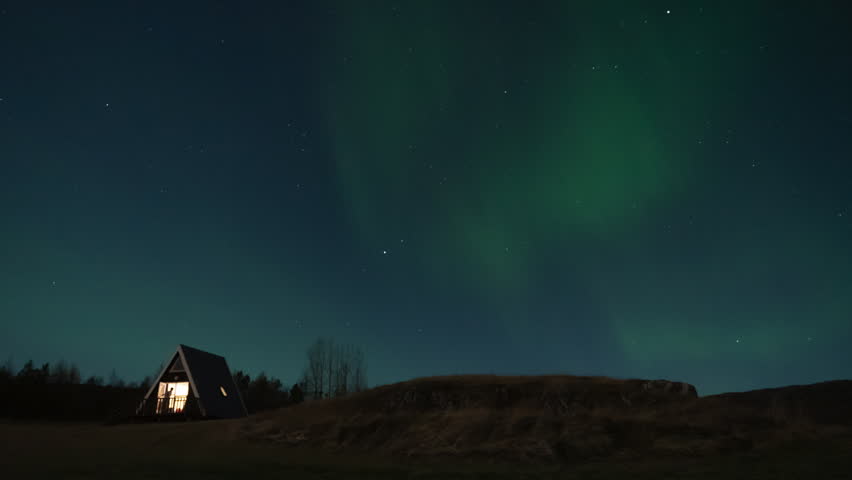 Timelapse of a Nordic cabin in Iceland beneath dancing Northern Lights illuminating the night sky over a peaceful remote landscape