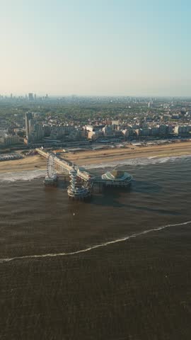 Aerial view of De Pier with its iconic Ferris wheel and observation tower stretching into the North Sea along the sandy beach and urban skyline of Den Haag, Zuid-Holland, Netherlands.