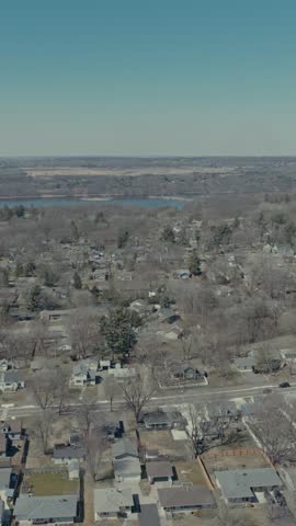 Aerial vertical parallax rise above suburban Hudson Wisconsin neighborhood showing dense housing among bare spring trees with St Croix River and long highway bridge beyond