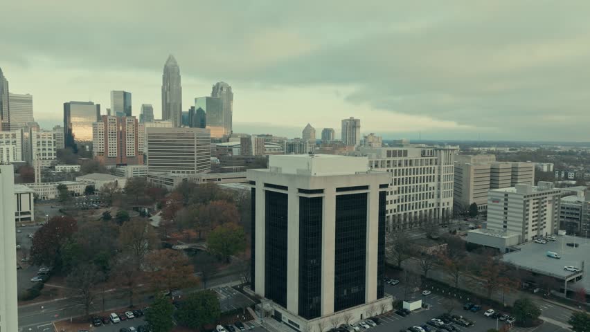 Aerial parallax orbit around the 13-story 301 Midtown office building on South McDowell Street revealing full Charlotte North Carolina skyline under moody overcast sky