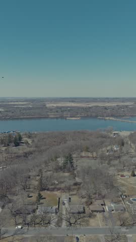 Aerial parallax shot above wooded Hudson Wisconsin bluff neighborhood revealing wide St Croix River, large marina with boat docks and winterized boats with flat farmland beyond