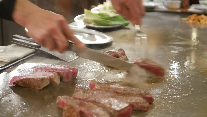 POV to kobe sirloin wagyu steak while cooking on teppan yaki flat pan in japanese style restaurant for lunch time. Chef cooking wagyu kobe beef sirloin steak on teppanyaki flat pan